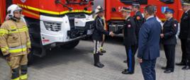 Na zdjęciu widać komendanta głównego PSP witającego się ze strażakiem OSP w stroju regionalnym.
W tle samochody pożarnicze i zebrani goście