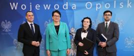 Konferencja na temat środków na realizację zadań w zakresie wychowania przedszkolnego dla Województwa Opolskiego na 2024 rok. Na zdjęciu od lewej: Dyrektor Biura Wojewody Jarosław Draguć, Wojewoda Opolski Monika Jurek, Opolski Kurator Oświaty Joanna Raźniewska oraz Dyrektor Wydziału Finansów i Budżetu Łukasz Krężel. Wszyscy stoją na tle niebieskiej ścianki z napisem "Wojewoda Opolski". 