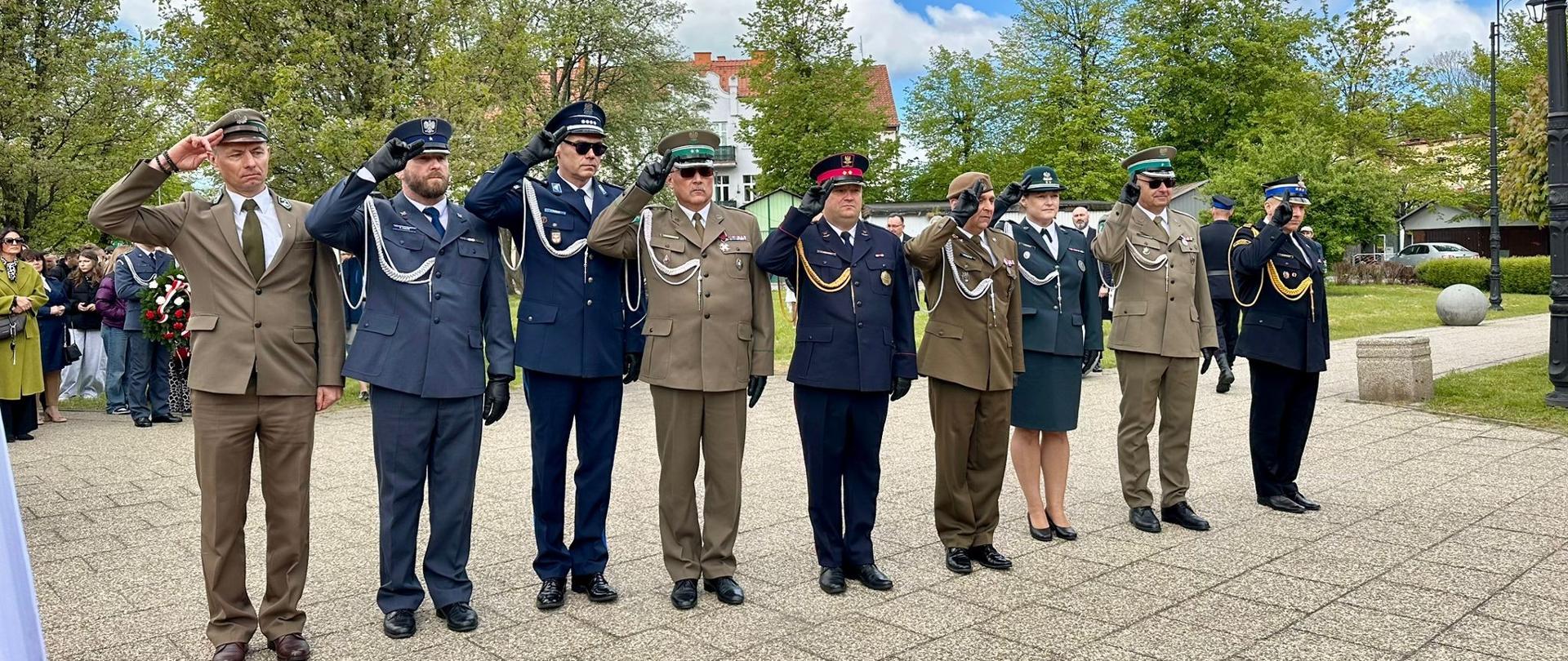 Na zdjęciu z prawej stoją przedstawiciele służb mundurowych w mundurach galowych, salutując do flagi.