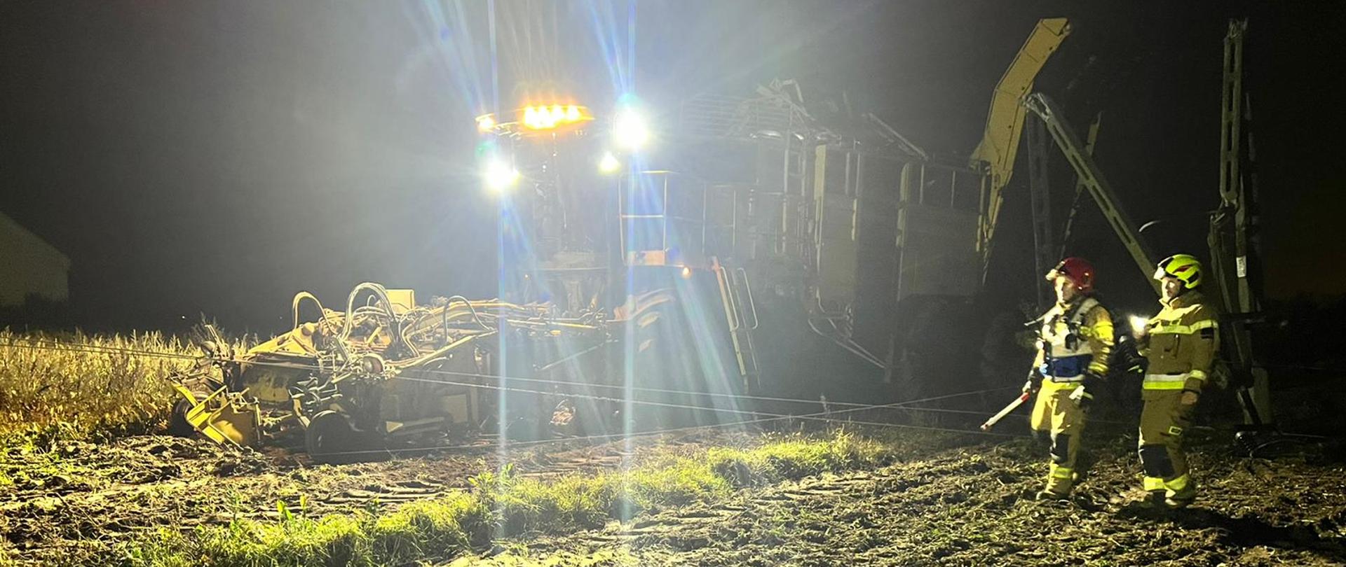 Na zdjęciu strażak na polu, obok stoi kombajn zaplątany w linie energetyczne 