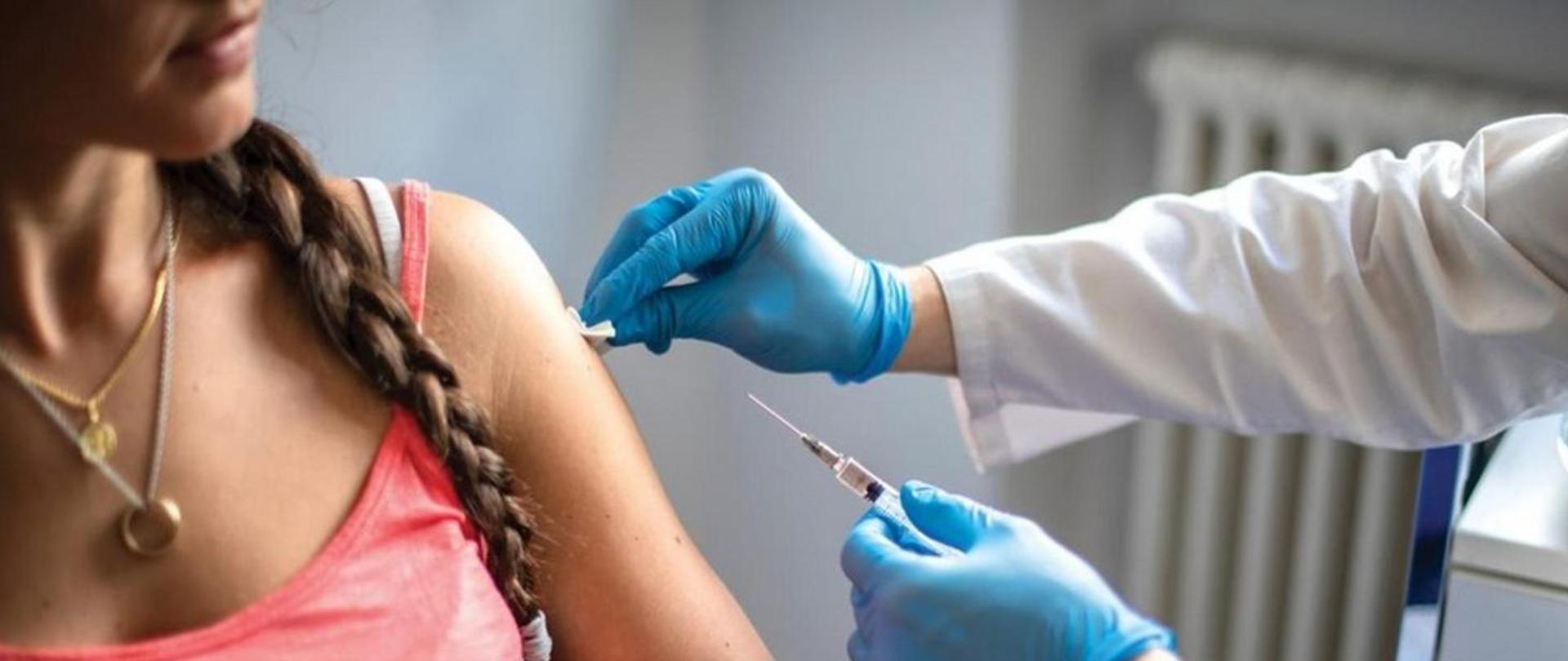 Na obrazku dziewczyna otrzymuje zastrzyk z szczepionką. 