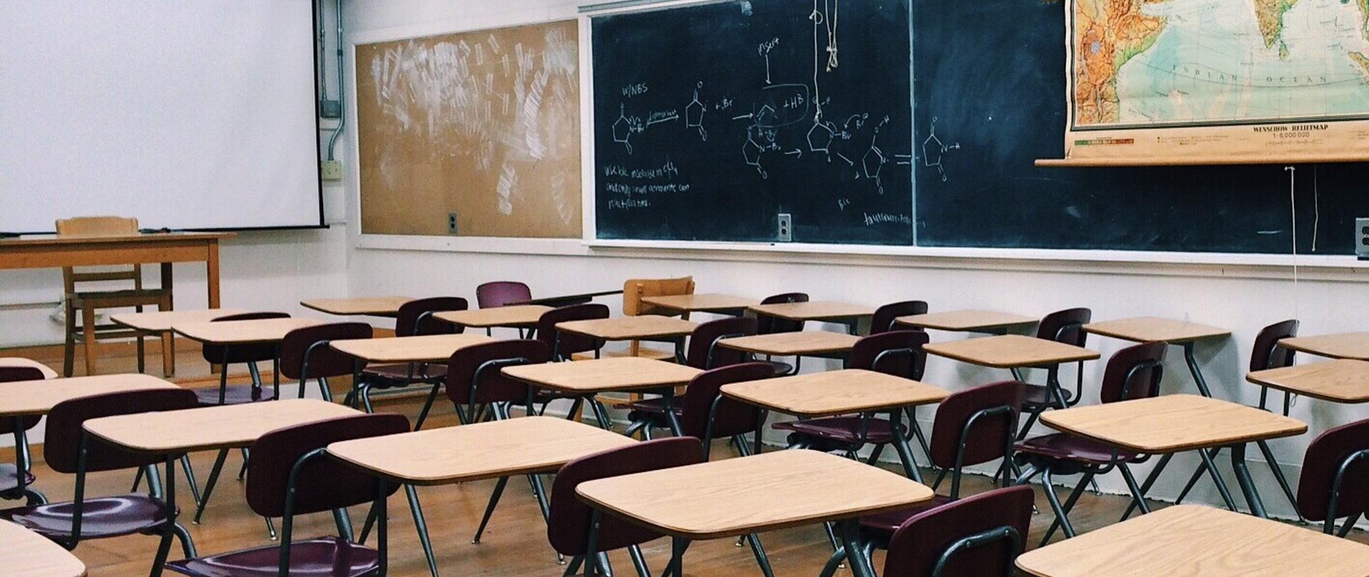 Klasa lekcyjna z ławkami dla uczniów i tablicami oraz mapą