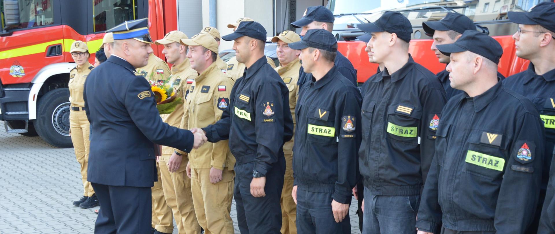 Plac przed komendą powiatową PSP. P.o. komendanta wita się z załogą komendy. 