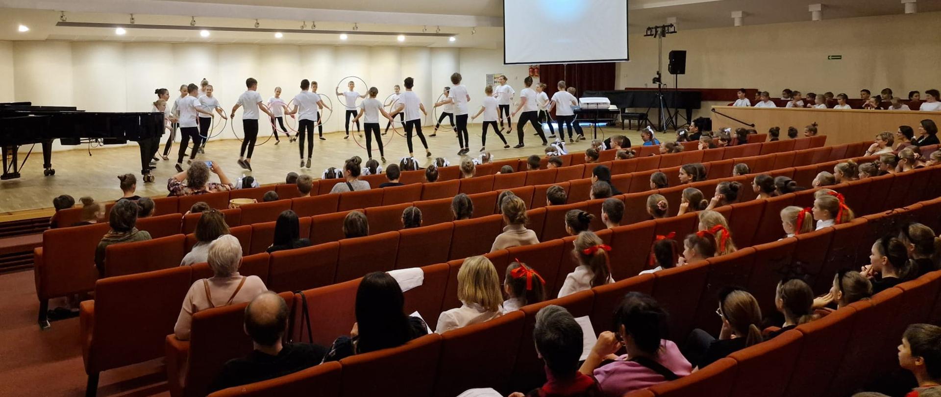 Duża grupa dzieci tańczy w kole z obręczami.