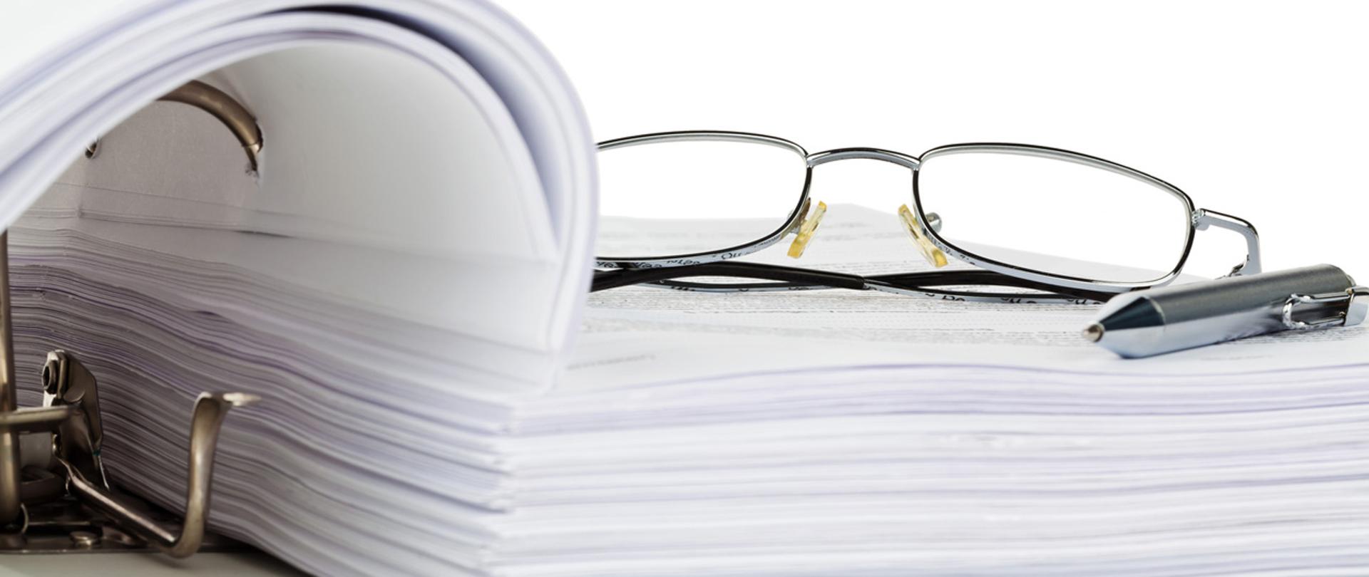 Okulary i długopis na otwartym segregatorze.