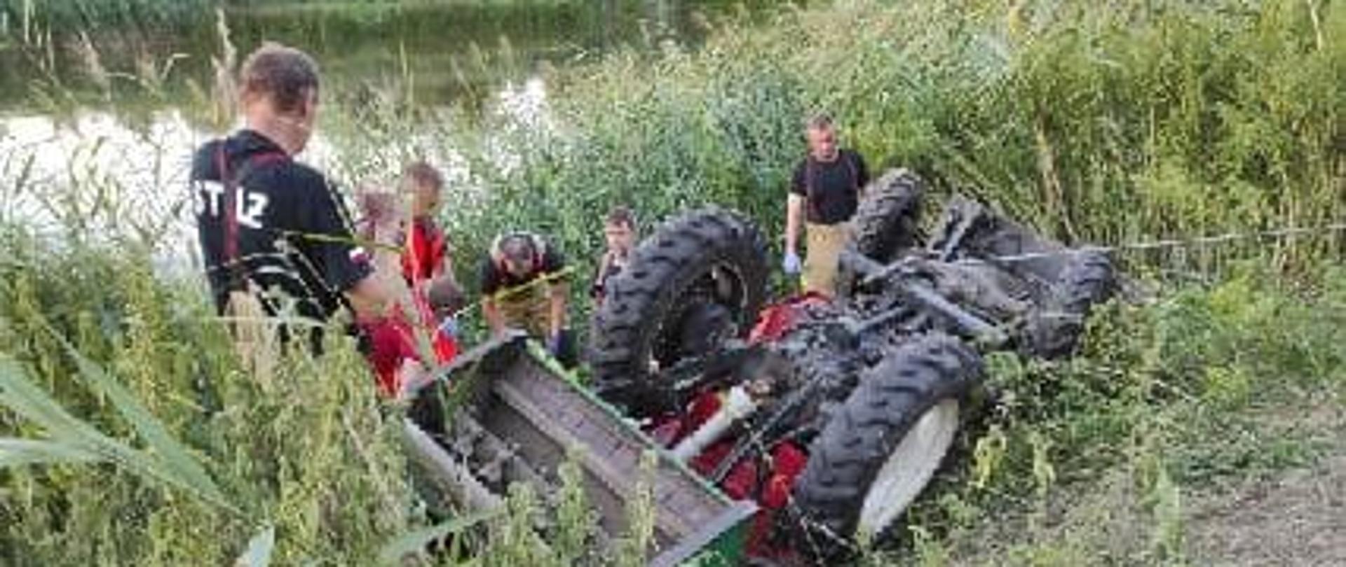 Przewrócony traktor ogrodniczym, pod którym znajduje się nieprzytomny mężczyzna w miejscowości Uścikówiec.