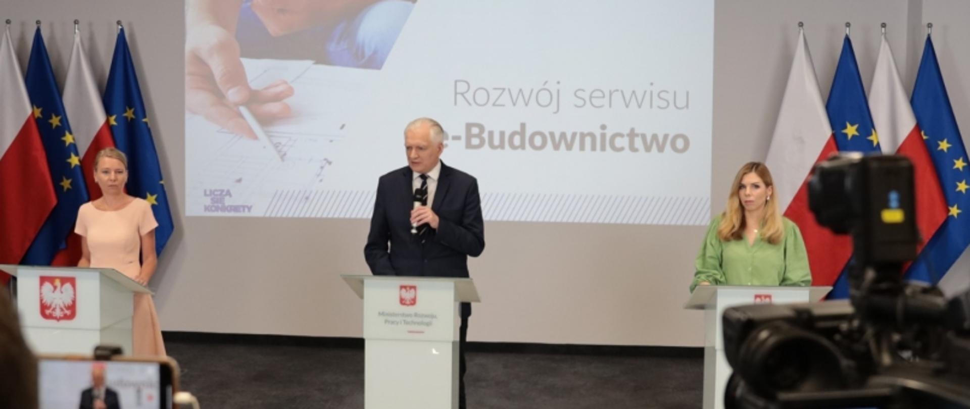 Prezentacja na temat rozwoju serwisu e-Budownictwo z udziałem trzech prelegentów, w tle ekran i flagi Polski oraz UE.