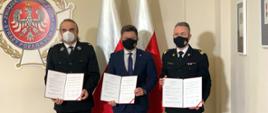 zdjęcie w siedzibie Zarządu Głównego Związku Ochotniczych Straży Pożarnych Rzeczypospolitej Polskiej Michała Dworczyka, szefa Kancelarii Prezesa Rady Ministrów(w środku), nadbrygadiera Andrzeja Bartkowiaka komendanta głównego PSP(z prawej) i druha Waldemara Pawlaka prezesa ZG ZOSP RP (z lewej). Każdy z Nich trzyma w rękach podpisane listy Intencyjne. W tle flagi Polski oraz logo Związków Ochotniczych Straży Pożarnych Rzeczypospolitej Polskiej