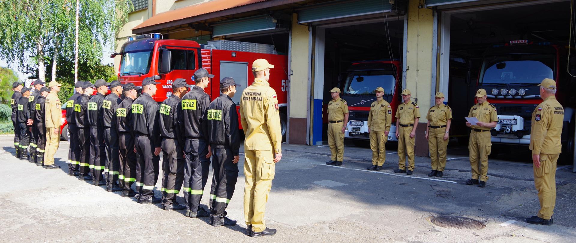 Zbiórka strażaków przed garażami JRG Wadowice. Na pierwszym planie, tyłem stoją strażacy JRG, na drugim planie – przodem – kadra kierownicza i dowódcza KP PSP Wadowice. W tle widoczny pojazd typu GCBARt przygotowany do wyjazdu do Grecji.