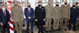 Zdjęcie zrobione w pomieszczeniu. Na zdjęciu w szeregu stoją uczestnicy uroczystości. Sześciu z nich ubranych w mundury: Wojska Polskiego, Państwowej Straży Pożarnej, Straży Granicznej i Policji. Dwóch mężczyzn ubranych jest w garnitury. W tle widać polski słup graniczny. 