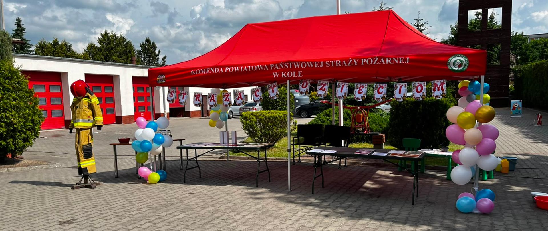 Zdjęcie przedstawia plac kolskiej komendy z przystrojonym balonami namiotem i napisem strażacy dzieciom