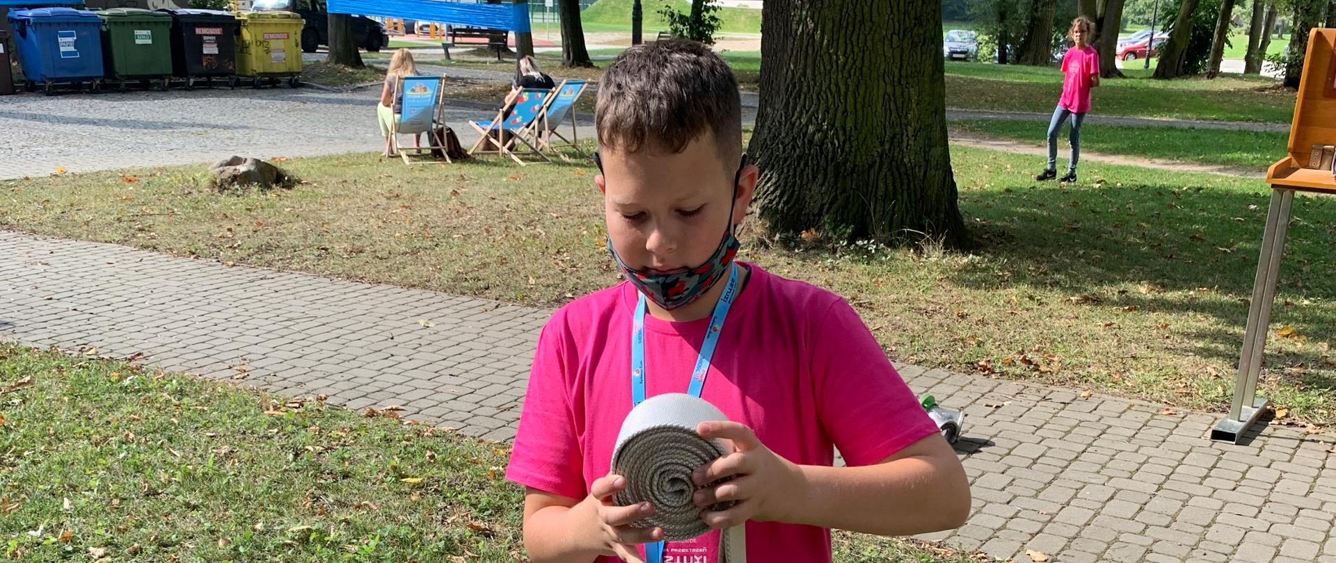 Dziecko zwija wąż strażacki w tle drzewo i inne osoby