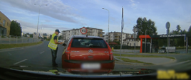 Umundurowany inspektor świętokrzyskiej ITD stoi obok samochodu osobowego zatrzymanego do kontroli drogowej i sprawdza trzeźwość kierującego przy użyciu alkomatu przesiewowego.