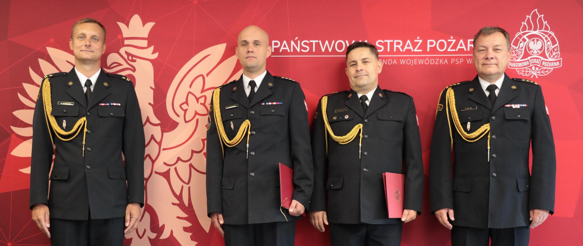 Zdjęcie pamiątkowe. Na zdjęciu widać Opolskiego Komendanta Wojewódzkiego PSP w Opolu, Komendanta Powiatowego PSP w Kędzierzynie-Koźlu, Zastępcę Komendanta Powiatowego PSP w Kędzierzynie-Koźlu oraz Naczelnika Wydziału w Wydziale Logistyki KW PSP w Opolu. Funkcjonariusze występują w umundurowaniu wyjściowym na tle loga PSP.