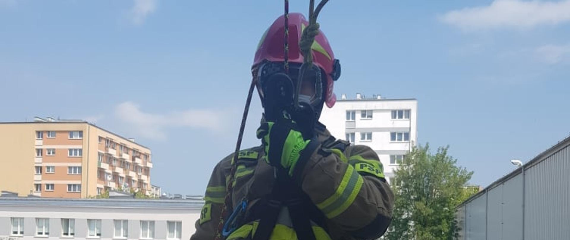 Strażak w ubraniu specjalnym zjeżdża na linie po ścianie wspinalni 