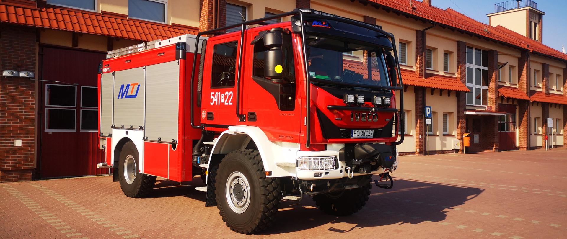 Na zdjęciu średni samochód gaśniczy marki IVECO przed budynkiem Jednostki Ratowniczo-Gaśniczej