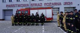Zakończenie szkolenia podstawowego Ochotniczych Straży Pożarnych. Na tle jednostki straży pożarnej ustawiony pojazd ratowniczy oraz pododdziały strażaków ratowników kończących szkolenie podstawowe oraz pododdział strażaków Państwowej Straży Pożarnej przygotowanych do zbiórki i podsumowania szkolenia. 