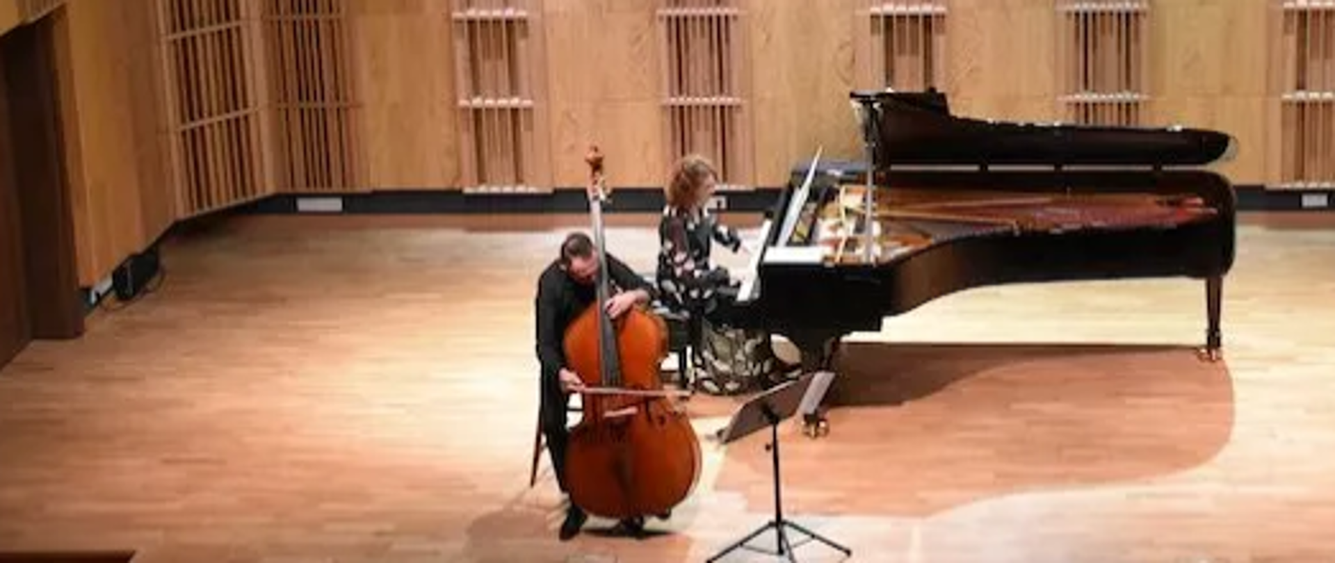 Zdjęcie przedstawia muzyków koncertujących W sali koncertowej szkoły muzycznej w Zambrowie. W centralnej części przy fortepianie gra pianistka wraz z kontrabasistą który jest przed nią. Oboje zajmują około połowę zdjęcia