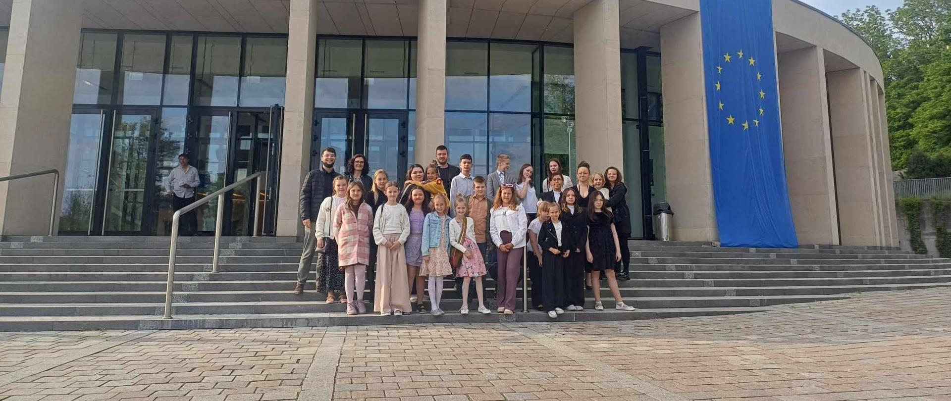 Uczestnicy wyjazdu stojący na schodach przed budynkiem Filharmonii Gorzowskiej.