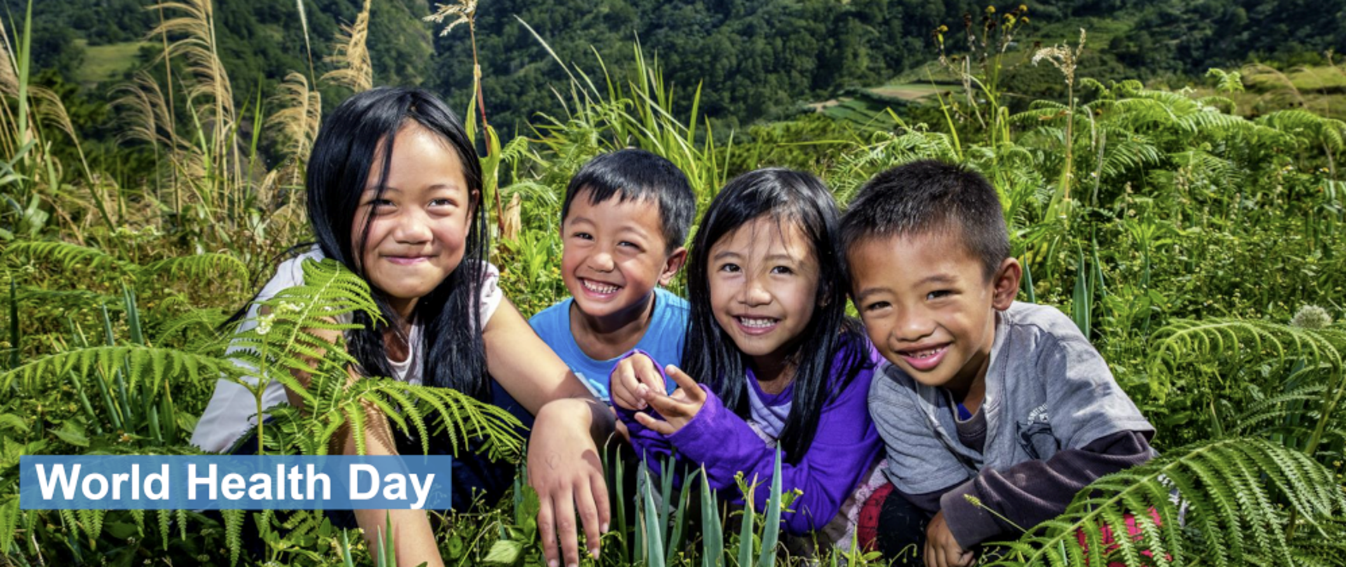 Czwórka uśmiechających się dzieci siedząca w trawie - po lewej napis "World Health Day"