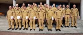 Pamiątkowe zdjęcie grupowe funkcjonariuszy PSP będących uczestnikami szkolenia z zakresu kierowania działaniami ratowniczymi na poziomie taktycznym (20 osób) w towarzystwie Zastępcy Komendanta Centralnej Szkoły PSP, kobiety oraz dwóch oficerów CS PSP