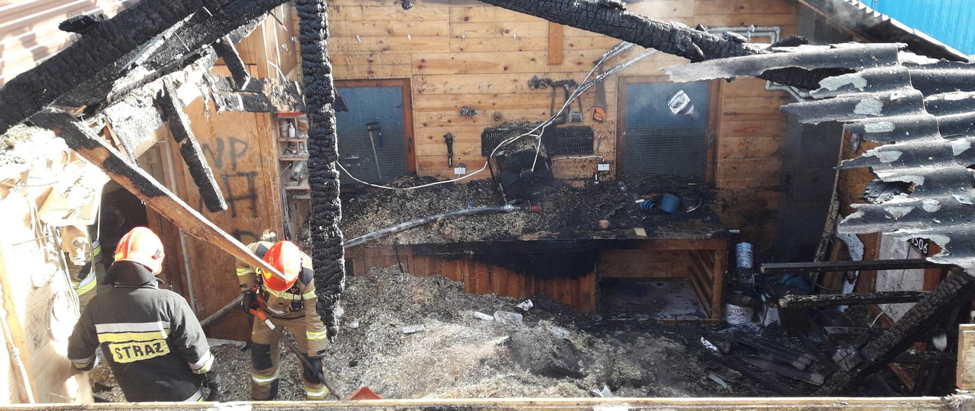 Widok spalonej stolarni oraz strażaków prowadzących działania.