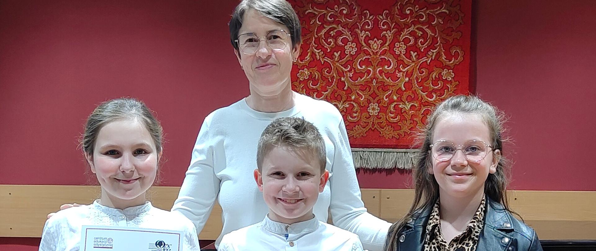 Zdjęcie przedstawia stojących troje uczniów szkoły, trzymających dyplomy, z nauczycielką Panią Małgorzatą Meyse