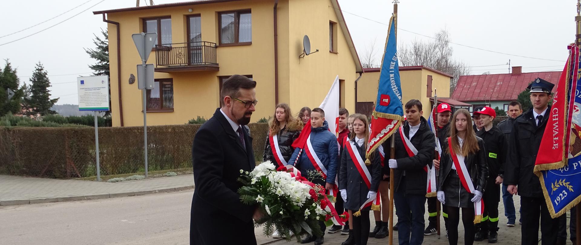 Na zdjęciu mężczyzna składa kwiaty pod tablica pamiątkową