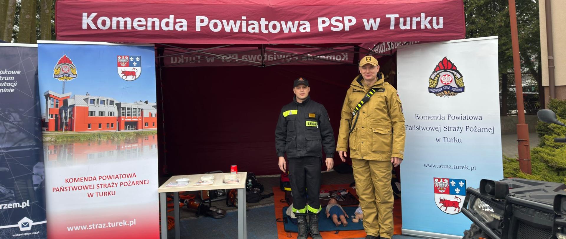 Strażacy stoją na pod namiotem, w którym eksponują sprzęt wykorzystywany podczas działań. 