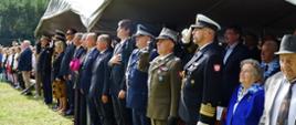 Zaproszeni goście stoją na baczność a przedstawiciele służb mundurowych oddają honor.