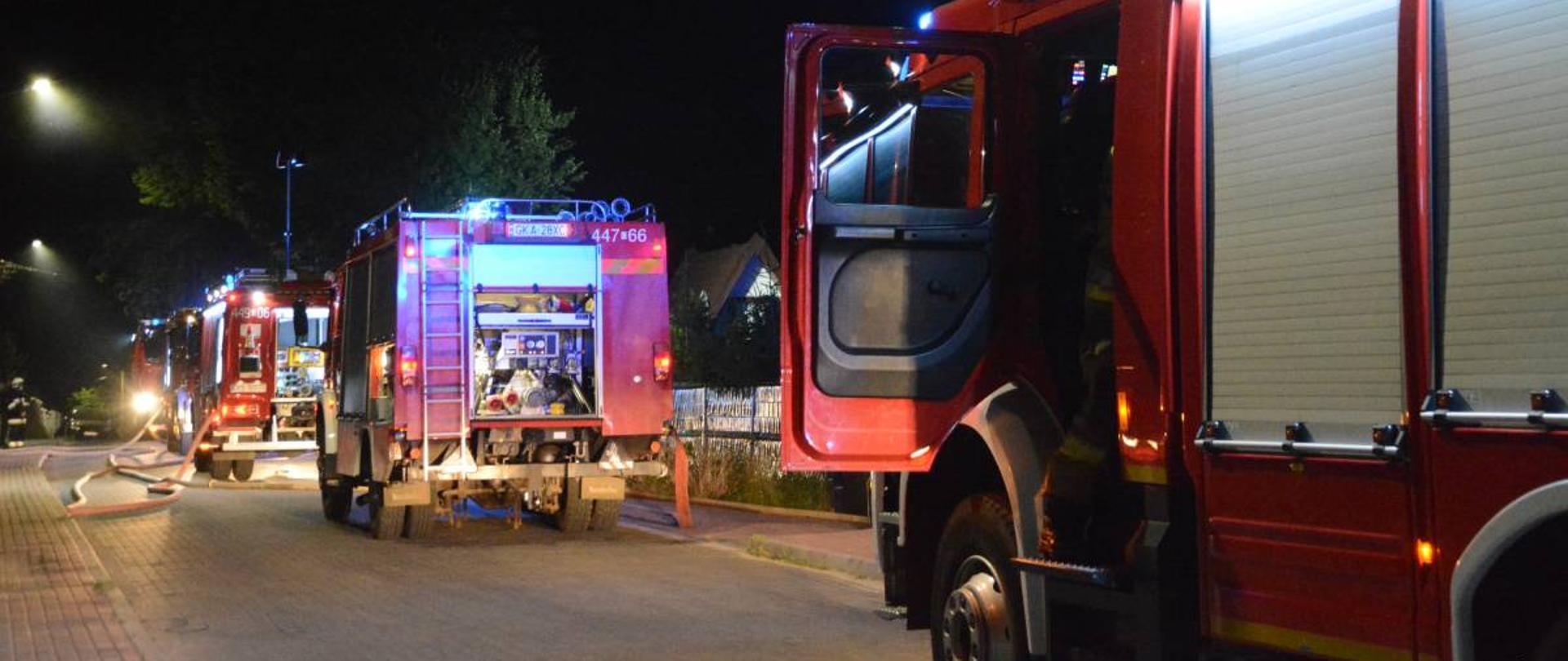 Ustawione w szeregu cztery samochody strażackie na drodze w pobliżu miejsca pożaru