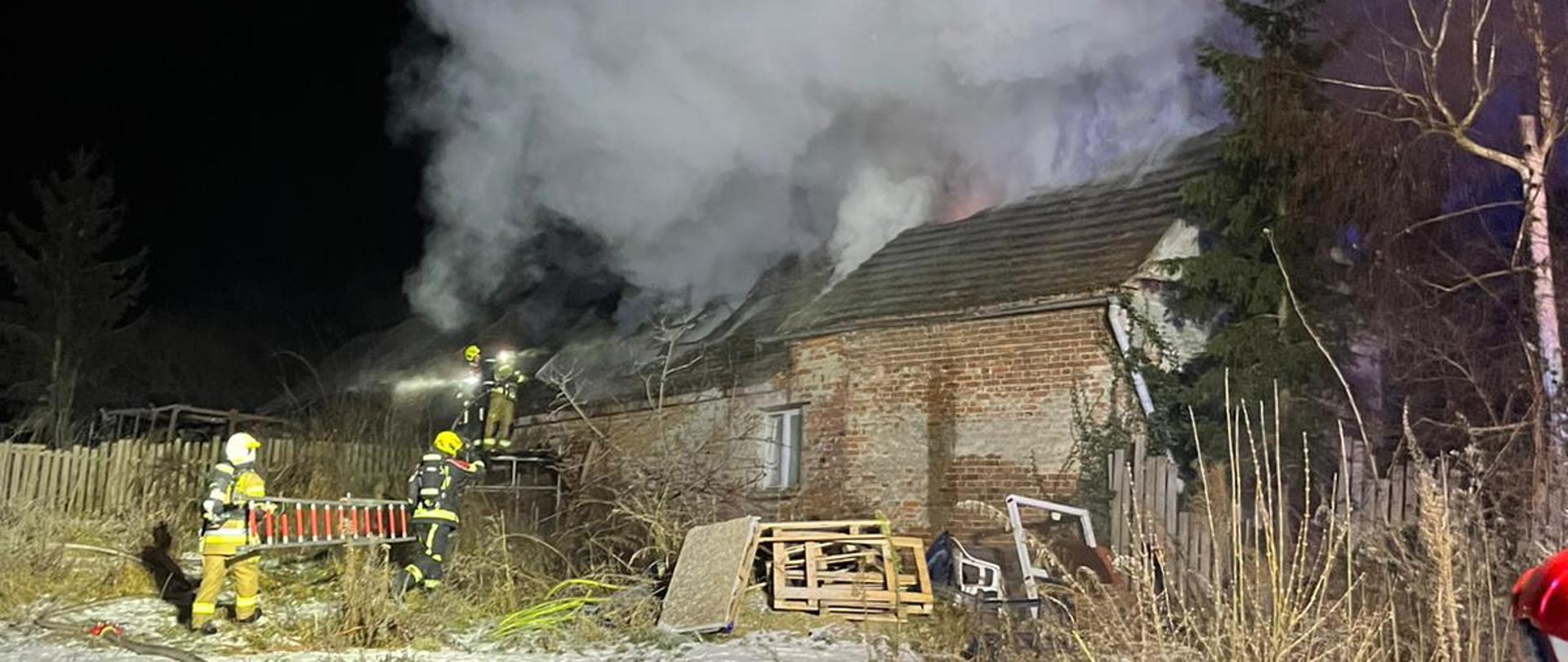 Pożar domu w m. Dąbrowa, strażacy gaszą pożar z zewnątrz budynku