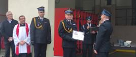 Pomorski komendant wojewódzki Państwowej Straży Pożarnej otrzymuje pamiątkę podczas uroczystości, za nim stoją zaproszeni goście.
