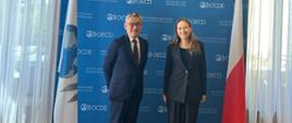 Minister funduszy i polityki regionalnej Katarzyna Pełczyńska-Nałęcz i Zastępca Sekretarza Generalnego OECD Yoshiki Takeuchi stoją, za ich plecami baner OECD oraz flagi Polski i OECD