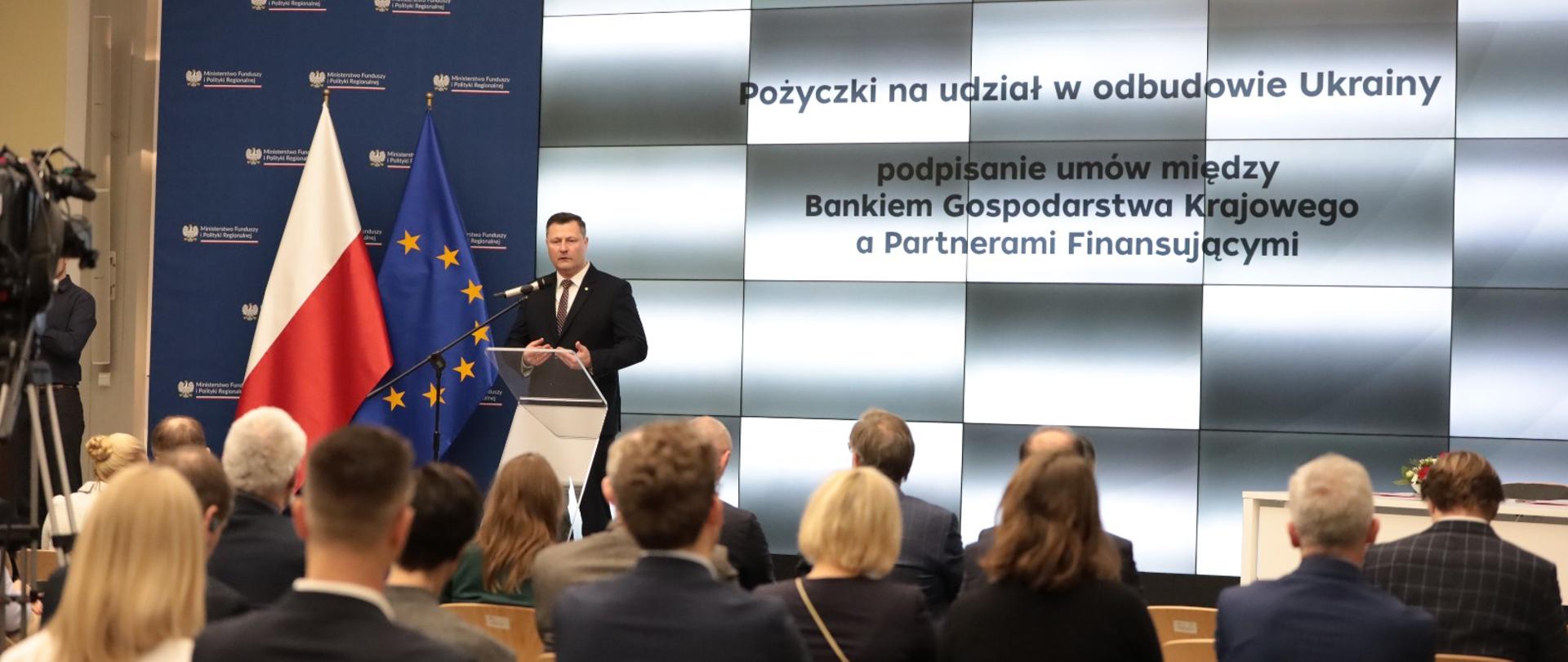 Minister Krzysztof Paszyk przemawia przy mównicy, w tle ekran multimedialny