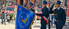 Poczet sztandarowy składający się ze strażaków maszeruje prezentując sztandar.
