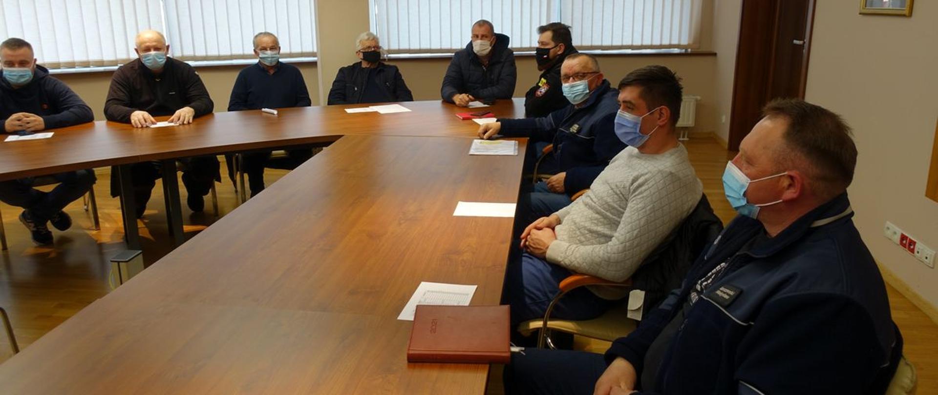 Komendanci Gminni w maseczkach siedzą przy stole w sali narad KM PS Nowy Sącz. 