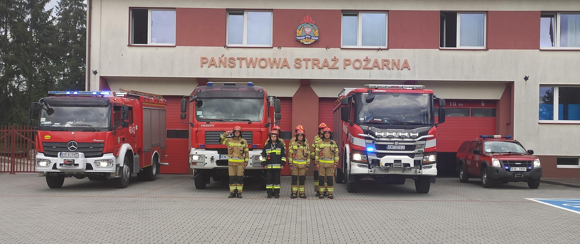 Na zdjęciu widoczni strażacy oddający hołd Powstańcom Warszawskim, w na tle samochodów pożarniczych oraz budynku JRG.