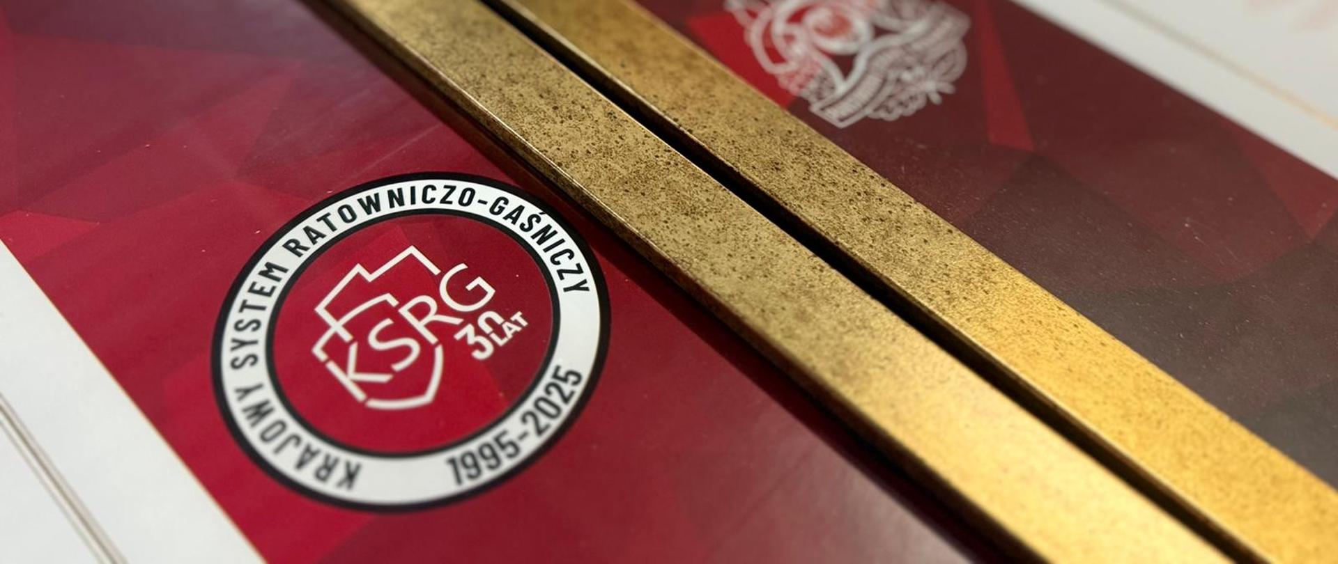 Na dyplomie w złotej ramce widoczne logo Krajowego Systemu Ratowniczo-Gaśniczego. 