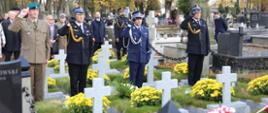 Na zdjęciu Komendant Centralnej Szkoły PSP w towarzystwie oficerów Policji, PSP oraz Wojska Polskiego salutują przed grobami stojąc w alejce cmentarnej
