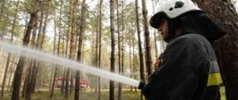 Zdjęcie przedstawia strażaka OSP podającego prąd wody w lesie