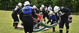 Zdjęcie przedstawia drużynę podczas startu bojowego w Zawody Sportowo-Pożarnicze w Słonowicach. Drużyna przy motopompie montuje węże ssawne oraz przygotowuje się do rozwinięcia linii głównej.