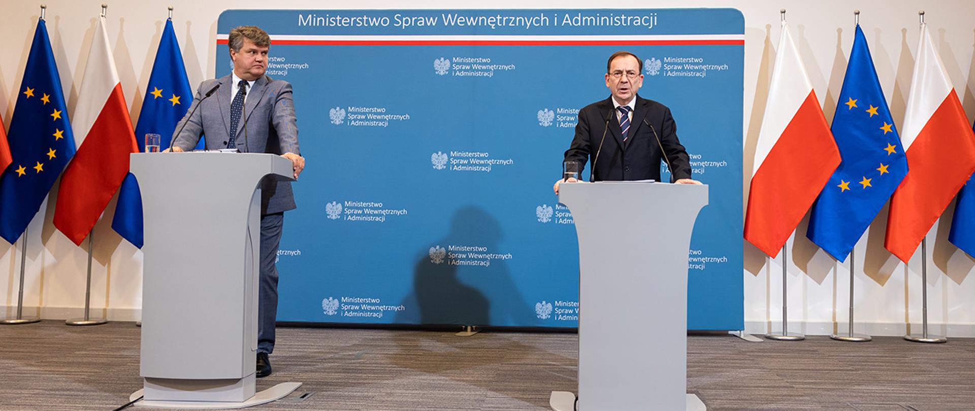 Na zdjęciu widać ministra Mariusza Kamińskiego i wiceministra Macieja Wąsika stojących za mównicami w trakcie konferencji prasowej.