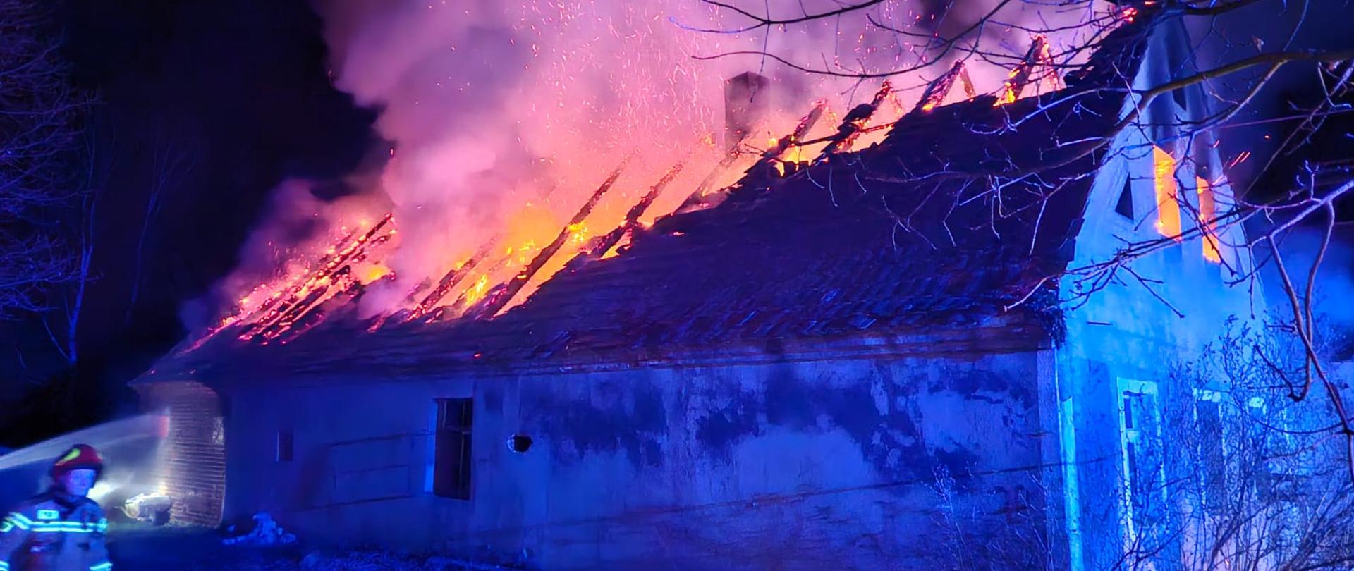 Strażacy gaszą płonący dach budynku.