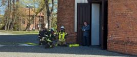 Na zdjęciu widzimy strażaków, którzy ubierają maski do aparatów powietrznych, w których będą wykonywali przeszukanie kościoła i ewakuację osoby poszkodowanej.