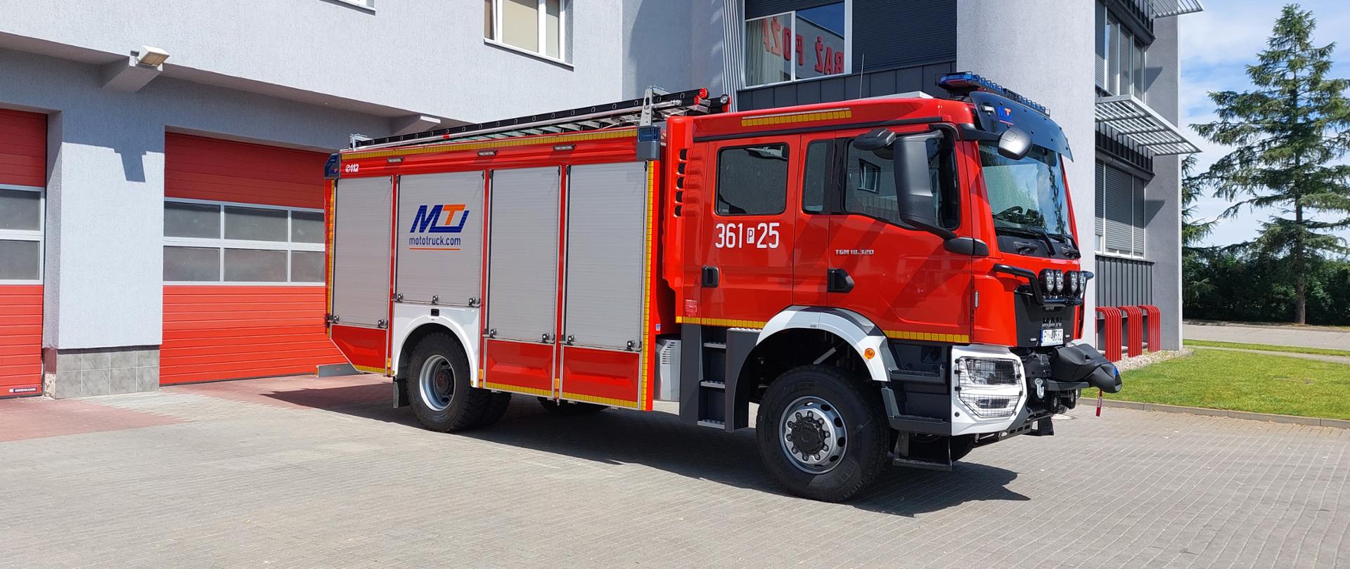 Zdjęcie przedstawia nowy ciężki samochód ratowniczo - gaśniczy, który stoi na placu przed budynkiem komendy 