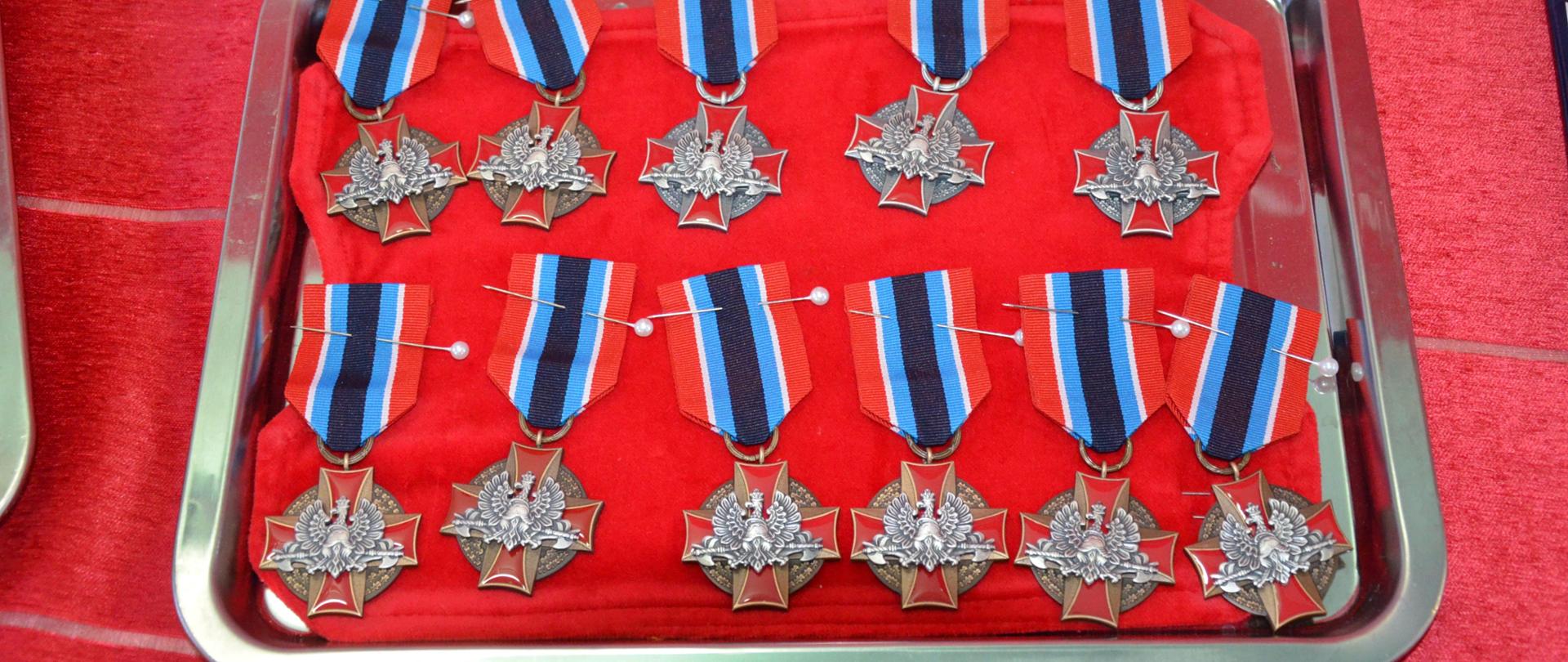 Zdjęcie przedstawia odznaczenia wręczane podczas uroczystości na ozdobnym czerwonym suknie