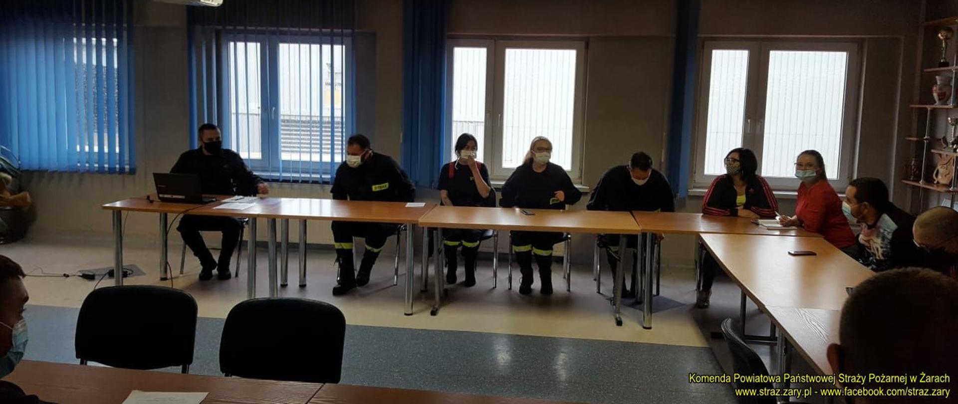 zajęcia szkoleniowe na kursie podstawowym strażaków ochotniczych straży pożarnych. Przy stole siedzą kursanci w maskach. Wykładowca prowadzi zajęcia na świetlicy w jednostce ratowniczo gaśniczej w Żarach. 