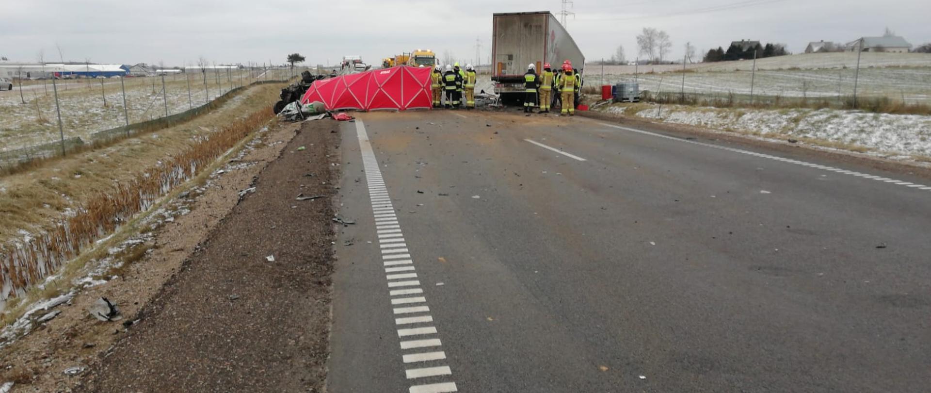 Na zdjęciu widoczny jest wrak samochodu ciężarowego, osobowego oraz strażaków podczas działań ratowniczo gaśniczych.